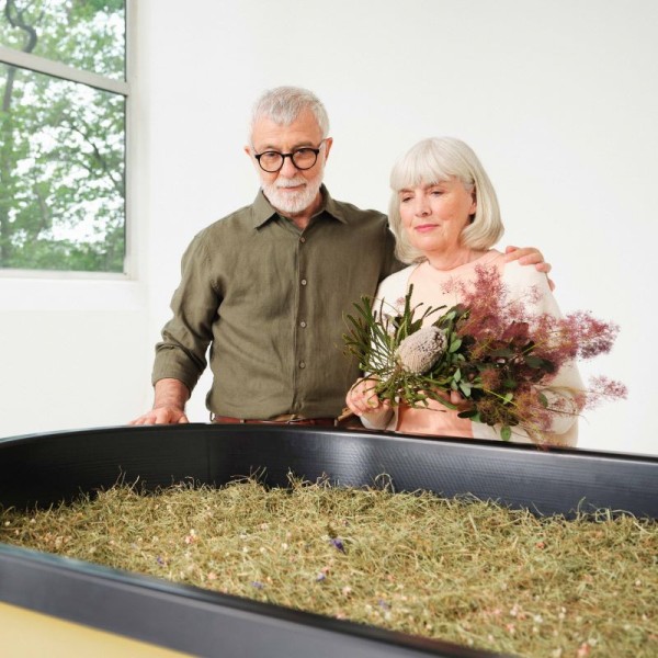 Personen stehen mit Blumen in den Händen über einem Kokon